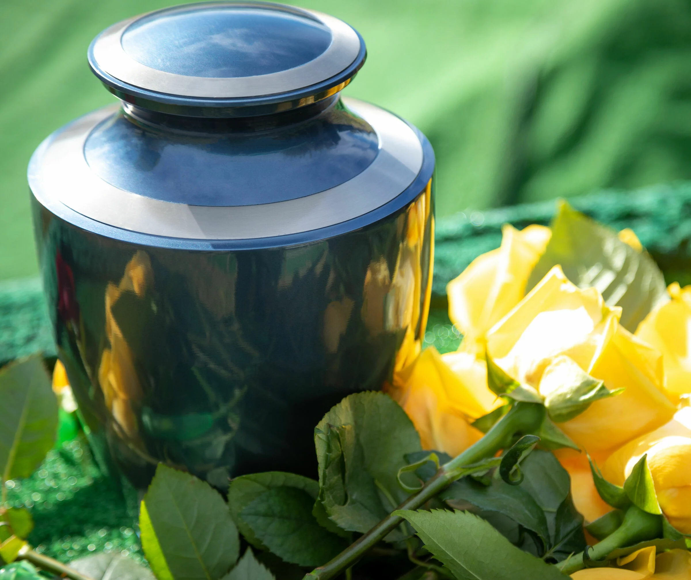 Dunkle Urne mit gelben Rosen steht an einem Urnengrab